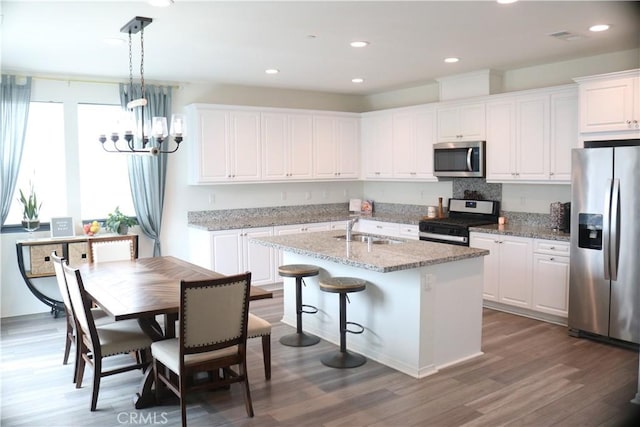 kitchen featuring wood finished floors, a kitchen island with sink, a sink, stainless steel appliances, and white cabinetry