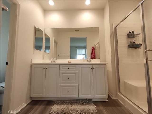 bathroom with double vanity, wood finished floors, a shower stall, and a sink