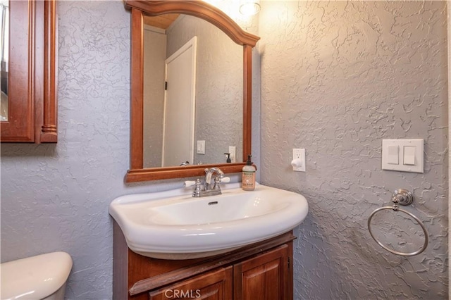 half bath featuring toilet, vanity, and a textured wall