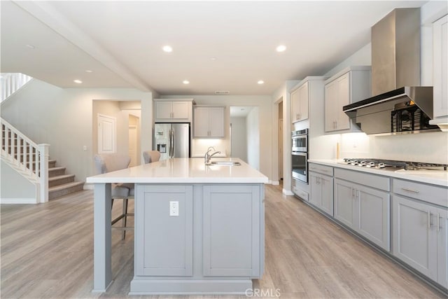 kitchen featuring light wood-style flooring, gray cabinets, a sink, stainless steel appliances, and wall chimney exhaust hood