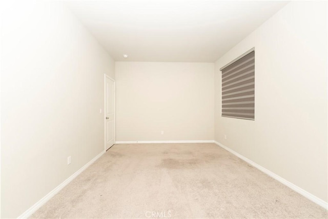 spare room featuring light colored carpet and baseboards