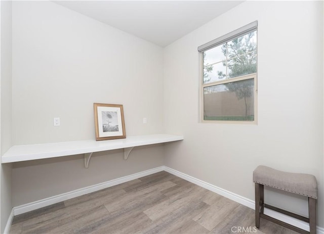 unfurnished office featuring baseboards, wood finished floors, and built in desk