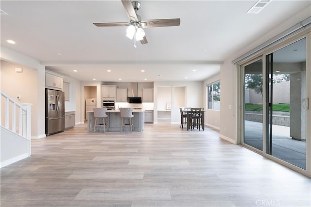 interior space featuring a breakfast bar, a kitchen island with sink, stainless steel appliances, light wood-style floors, and light countertops