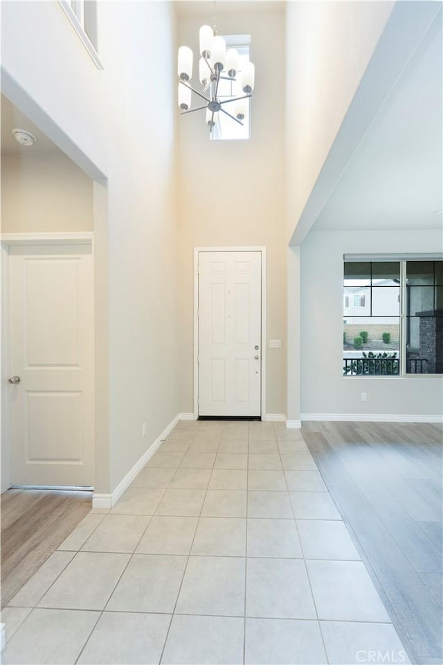 foyer featuring light tile patterned floors, a notable chandelier, baseboards, and a towering ceiling