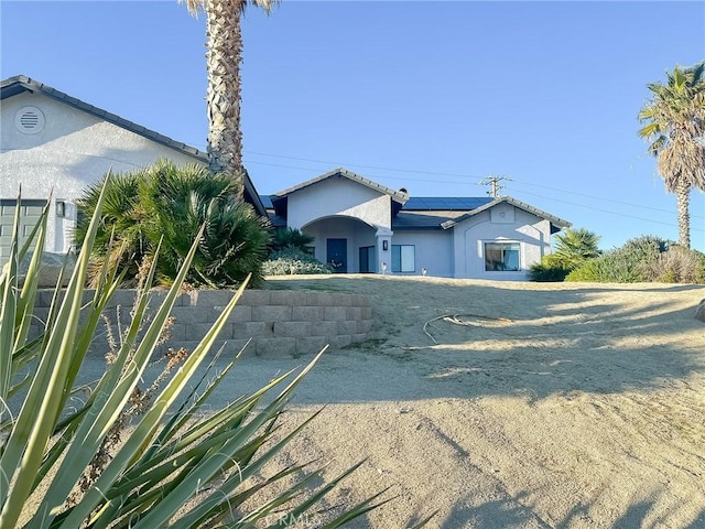 ranch-style home with roof mounted solar panels and stucco siding