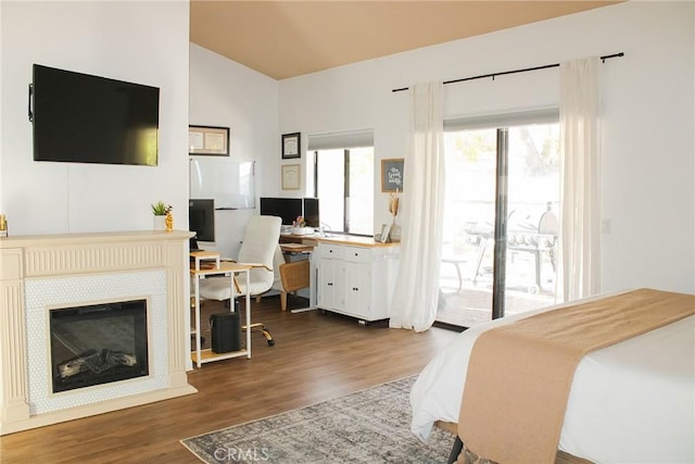 bedroom with a glass covered fireplace, wood finished floors, vaulted ceiling, and access to outside