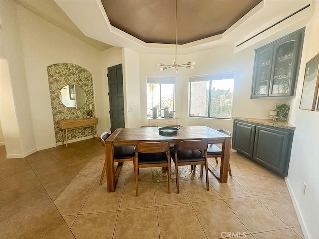 dining space featuring a raised ceiling, a notable chandelier, light tile patterned floors, and baseboards