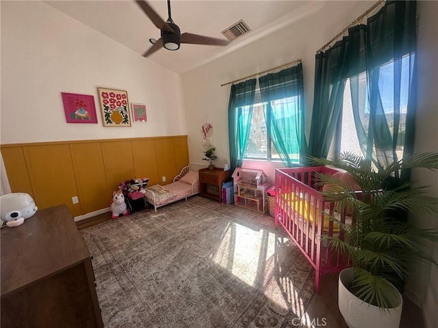 bedroom with a wainscoted wall, visible vents, lofted ceiling, ceiling fan, and a decorative wall