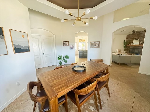 dining room with a tray ceiling, light tile patterned floors, arched walkways, and a large fireplace