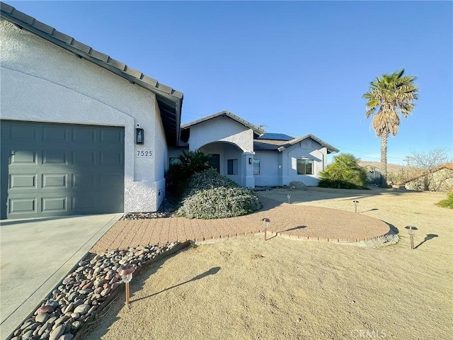 view of front of home featuring solar panels, an attached garage, driveway, and stucco siding