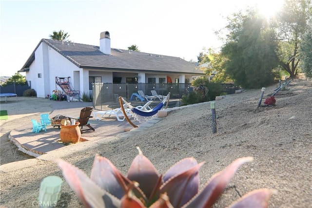 back of house featuring a trampoline, an outdoor fire pit, a patio area, a chimney, and a tiled roof