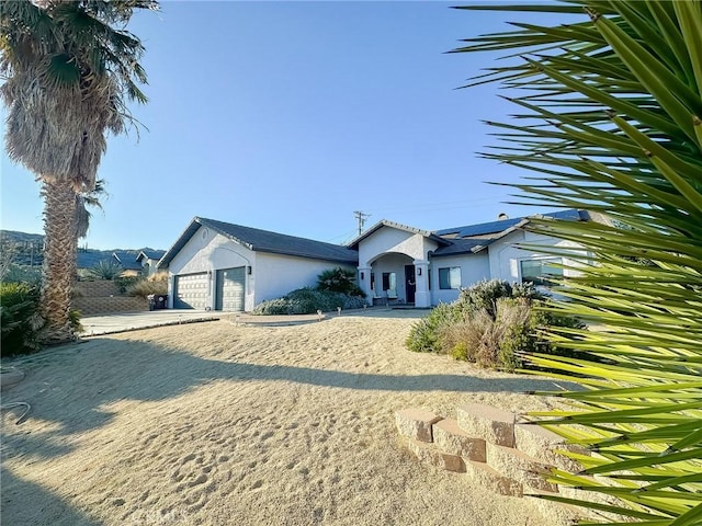 view of front facade with roof mounted solar panels, stucco siding, and a garage