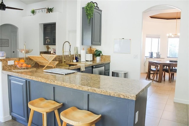 kitchen with a kitchen bar, arched walkways, a peninsula, light tile patterned floors, and dishwasher