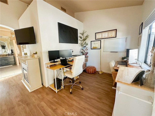 office area with visible vents, arched walkways, light wood finished floors, and baseboards