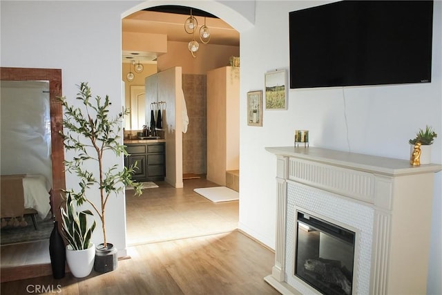 living area with arched walkways, light wood-style flooring, and a tiled fireplace