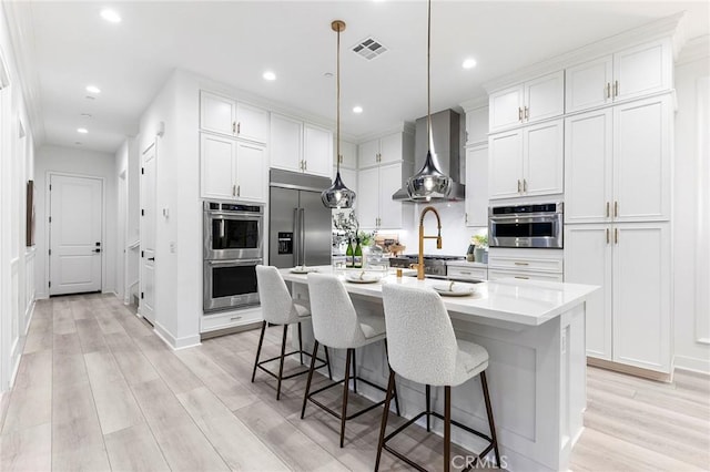 450 Chorus, Irvine, CA 92618 - kitchen featuring visible vents, wall chimney range hood, a breakfast bar area, light wood-style floors, and stainless steel appliances
