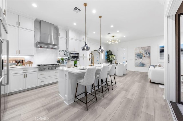 450 Chorus, Irvine, CA 92618 - kitchen with an island with sink, wall chimney range hood, white cabinetry, stainless steel appliances, and light countertops