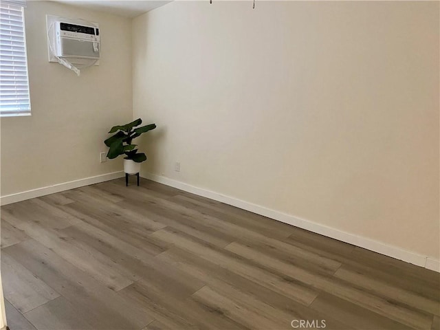 unfurnished room featuring wood finished floors, baseboards, and a wall mounted air conditioner