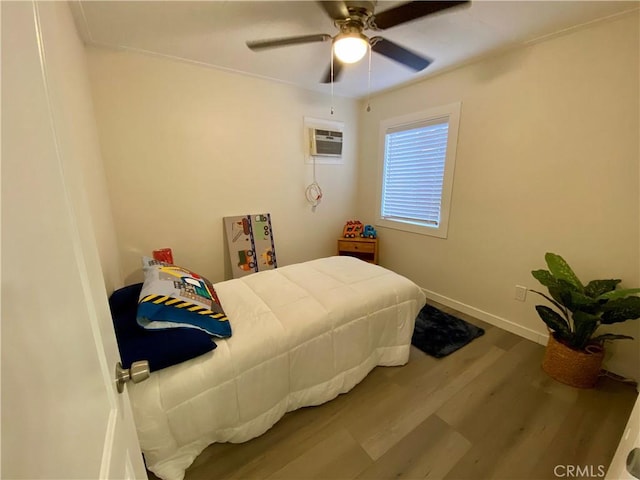 bedroom with baseboards, a ceiling fan, a wall unit AC, and wood finished floors