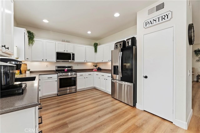 29193 Via Espada, Murrieta, CA 92563 - kitchen featuring appliances with stainless steel finishes, white cabinetry, dark countertops, light wood-type flooring, and recessed lighting