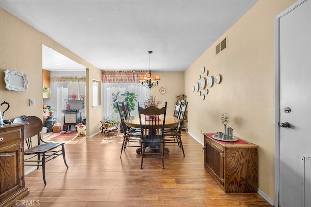 dining area with visible vents, light wood-style flooring, an inviting chandelier, and baseboards