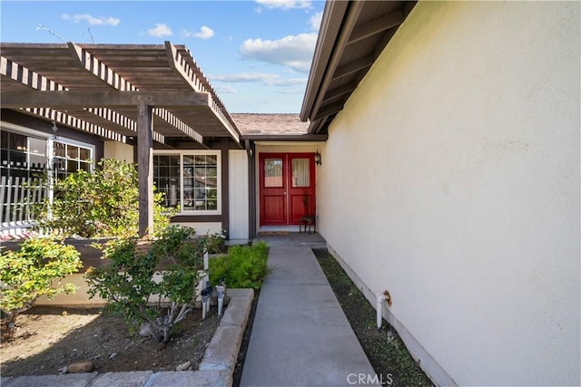 view of exterior entry with stucco siding and a pergola