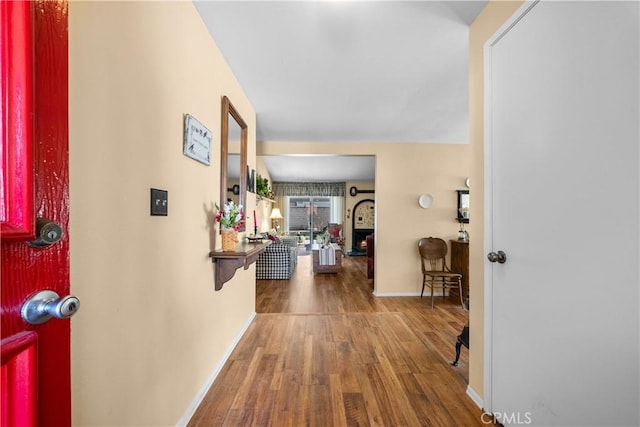 entryway with a warm lit fireplace, baseboards, and wood finished floors