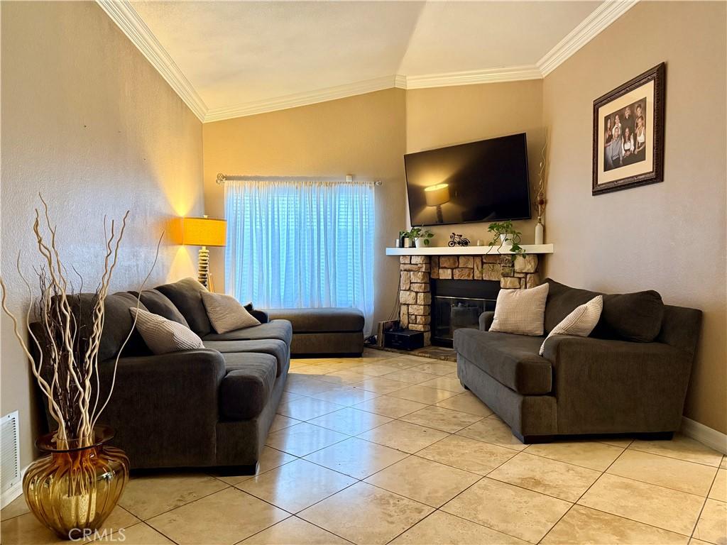 living room featuring vaulted ceiling, light tile patterned floors, a fireplace, and ornamental molding