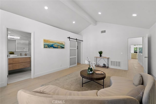 living area with lofted ceiling with beams, a barn door, light wood-type flooring, and visible vents