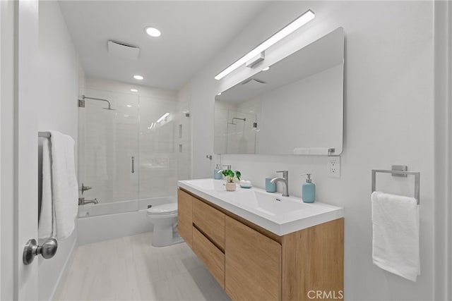 bathroom featuring toilet, a sink, recessed lighting, double vanity, and enclosed tub / shower combo