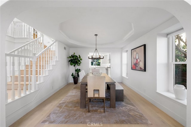 dining room with a tray ceiling, arched walkways, light wood finished floors, and a chandelier