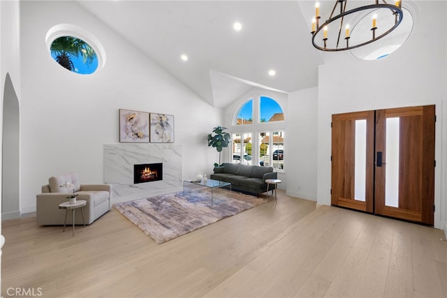 living area with a premium fireplace, recessed lighting, wood finished floors, a notable chandelier, and high vaulted ceiling