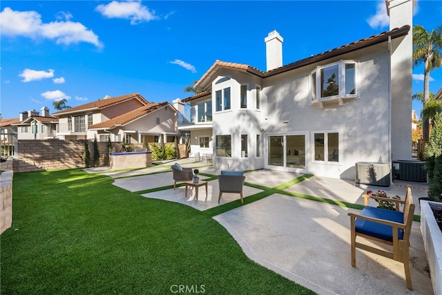 back of house featuring stucco siding, cooling unit, a chimney, a lawn, and a patio area