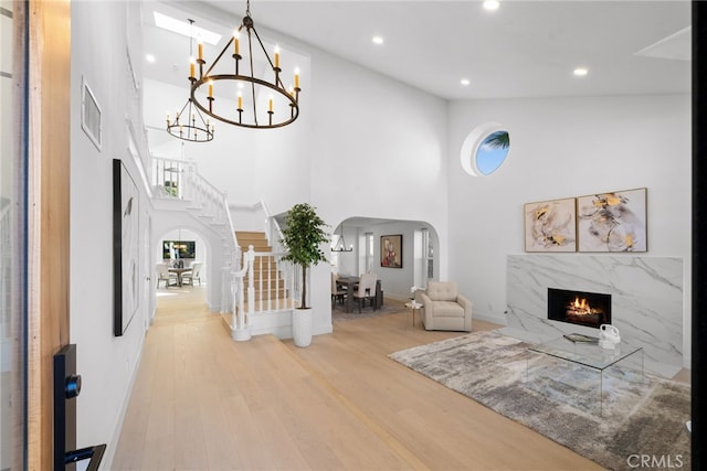 living room featuring wood finished floors, a premium fireplace, a high ceiling, arched walkways, and stairs