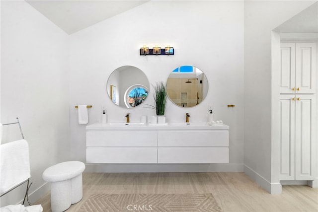 full bath with double vanity, vaulted ceiling, baseboards, and a sink