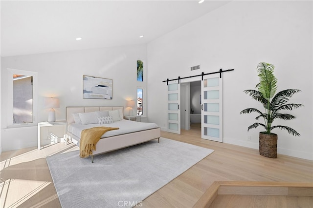 bedroom with wood finished floors, visible vents, high vaulted ceiling, recessed lighting, and a barn door