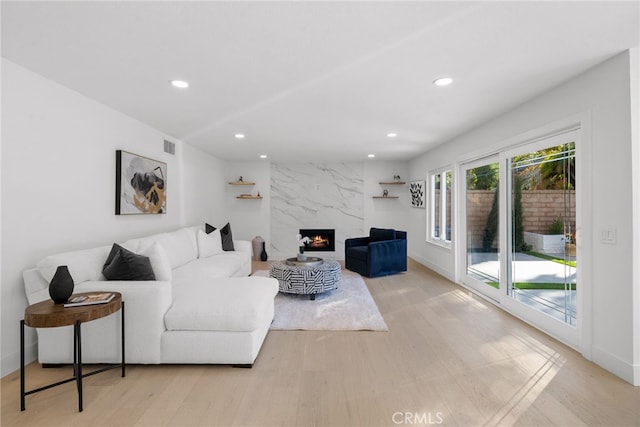 living room with recessed lighting, a premium fireplace, baseboards, and light wood-style flooring