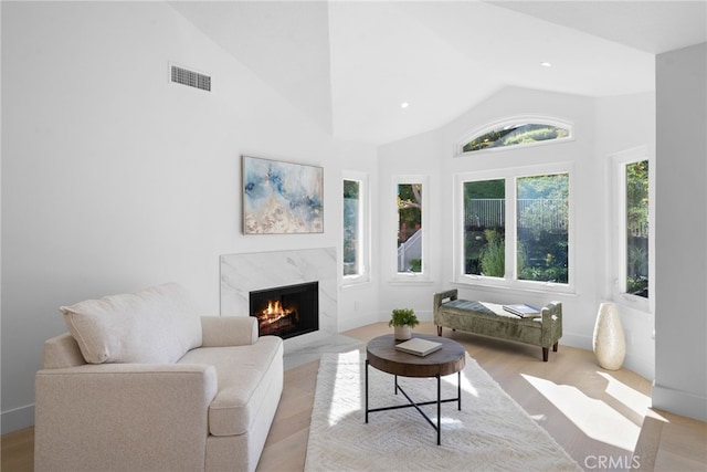 living room featuring wood finished floors, visible vents, a high end fireplace, and high vaulted ceiling