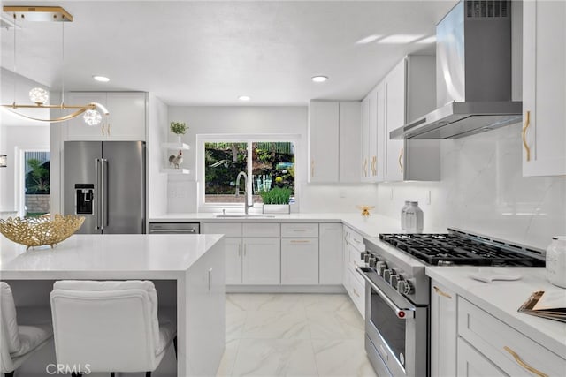 kitchen featuring marble finish floor, a sink, premium appliances, backsplash, and wall chimney exhaust hood