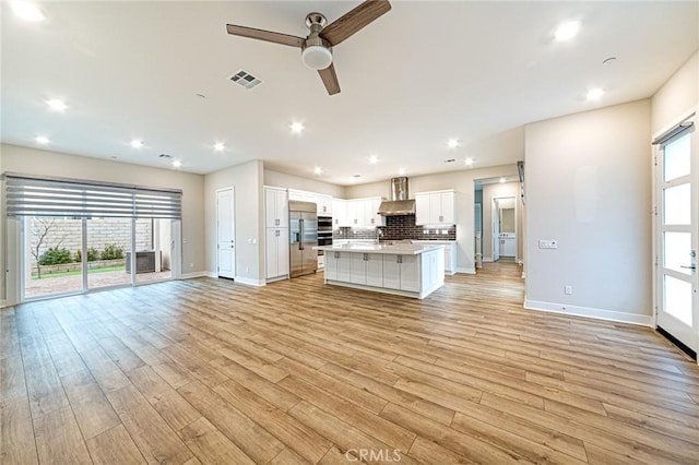 kitchen with visible vents, stainless steel appliances, white cabinetry, wall chimney range hood, and open floor plan