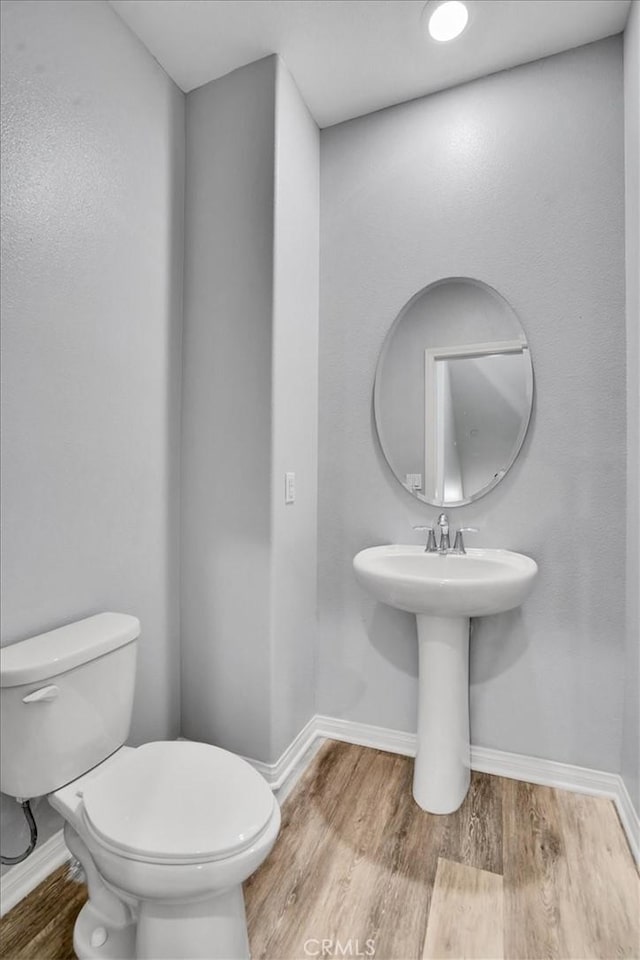 half bath featuring baseboards, toilet, and wood finished floors