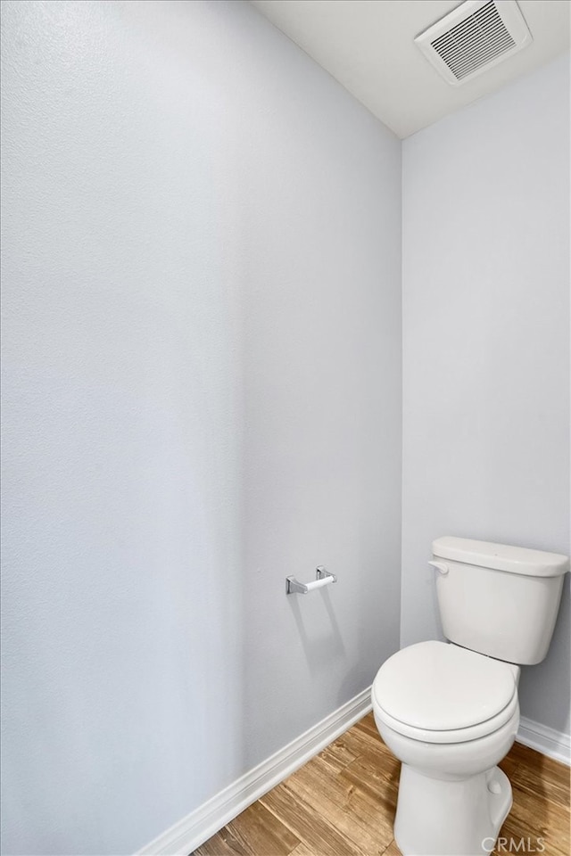 bathroom featuring toilet, wood finished floors, visible vents, and baseboards