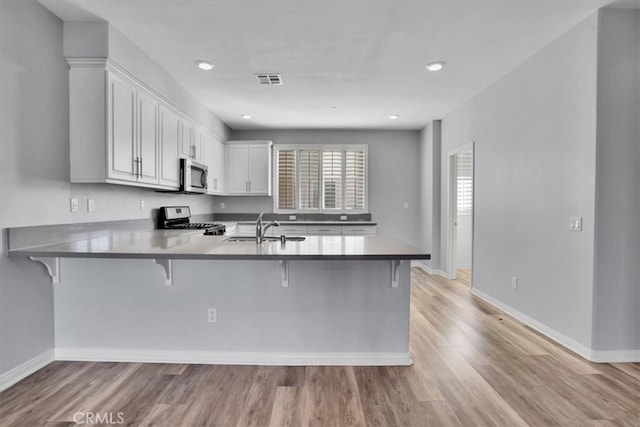 kitchen featuring a breakfast bar, a peninsula, light wood-style floors, stainless steel appliances, and a sink