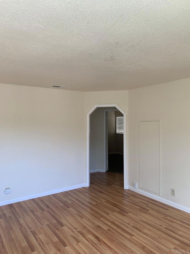 spare room with arched walkways, light wood finished floors, a textured ceiling, and baseboards