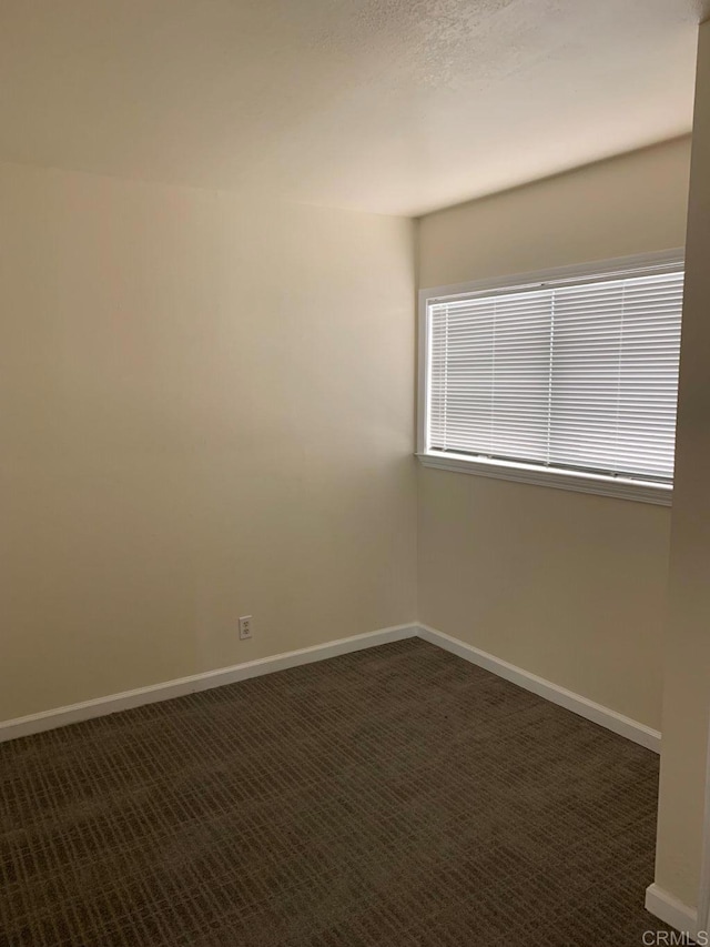 empty room featuring dark colored carpet and baseboards