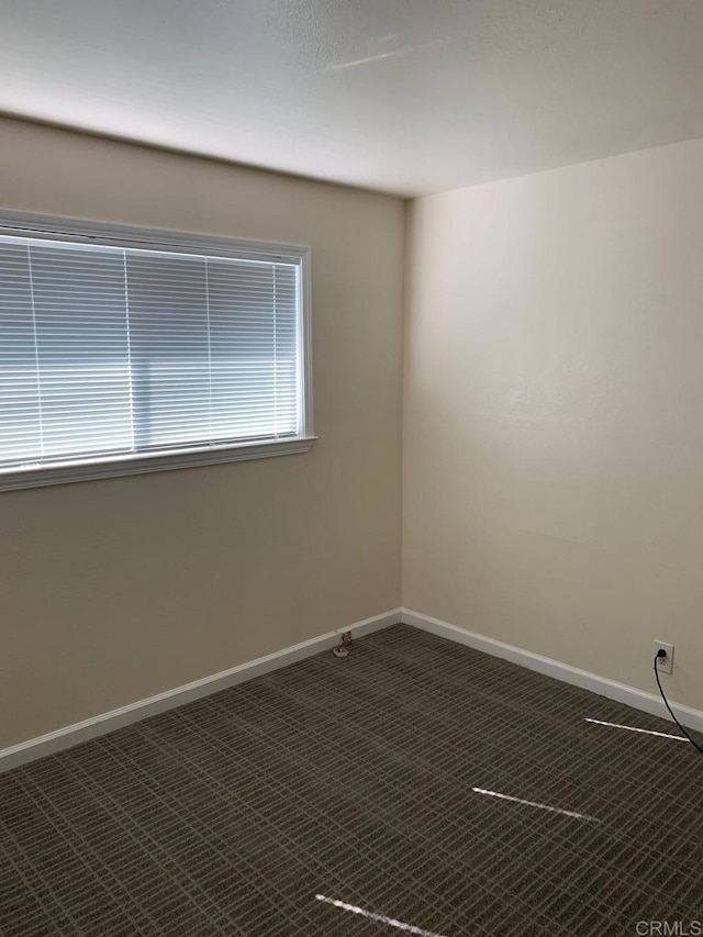 empty room featuring baseboards and dark carpet