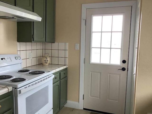 kitchen with tile countertops, electric stove, under cabinet range hood, green cabinets, and backsplash