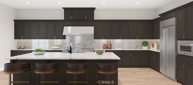 9547 N Andora Ave, Chatsworth, CA 91311 - kitchen featuring range hood, decorative backsplash, an island with sink, light wood finished floors, and light stone counters