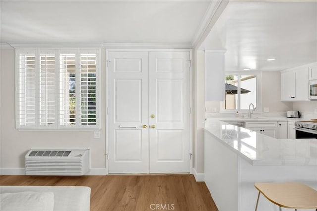 kitchen with light wood-type flooring, a wall unit AC, a breakfast bar area, white cabinets, and light countertops