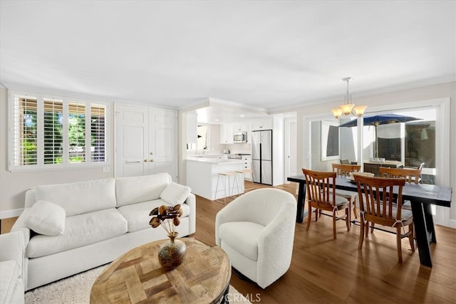 living area with a chandelier, baseboards, wood finished floors, and ornamental molding